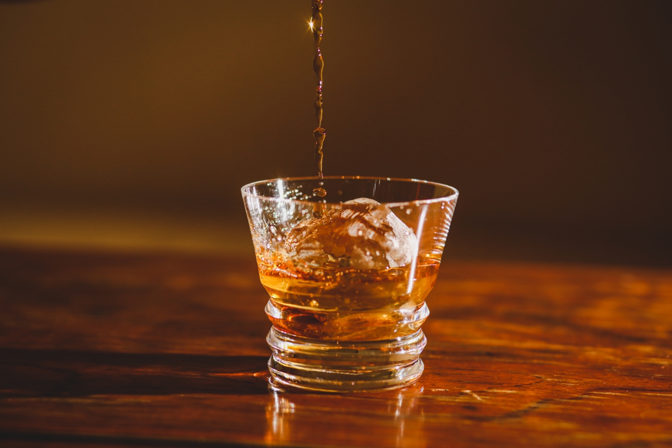 画像：グラスに氷が入っていて、ウイスキーの液を上部から入れている様子。